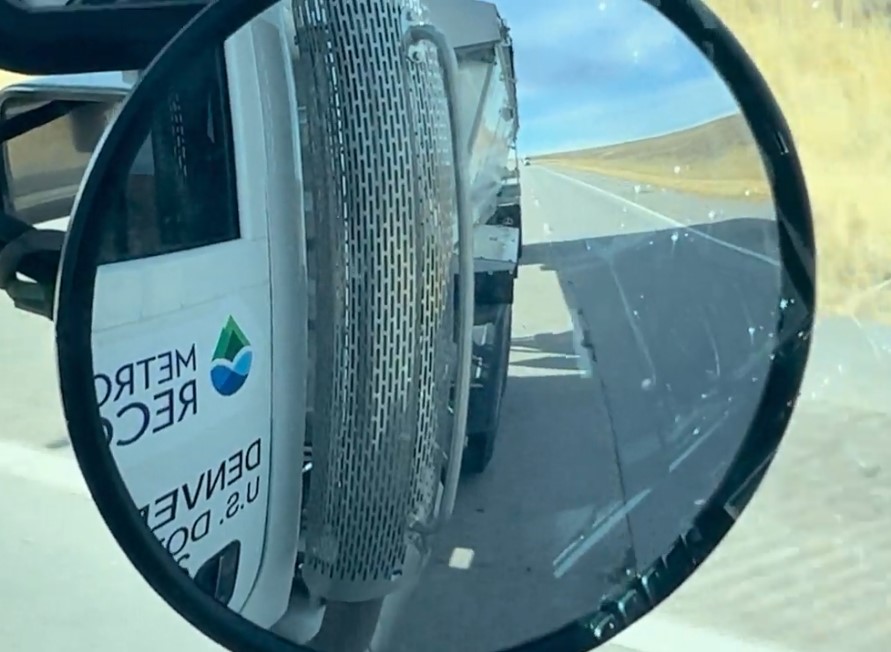 A side-view mirror reflecting the METROGRO truck while driving